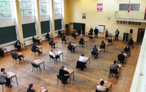 Zdjęcie podczas egzaminu na auli szkolnej. Komisja informuje uczniów o zasadach obowiązujących na egzaminie.