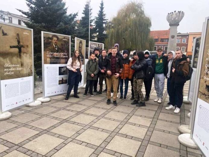 Uczniowie podczas nietypowej lekcji oglądają plenerową wystawę nt. historii Polski.