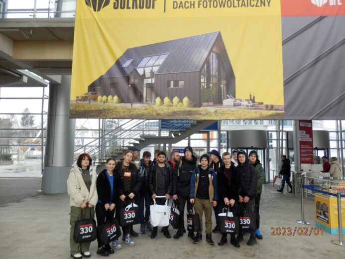 Targi budownictwa "BUDMA 2023"- zdjęcie grupowe przy banerze firmy produkujące dachy fotowoltaiczne.