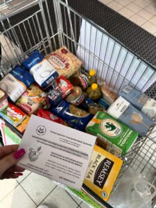 Na zdjęciu widać koszyk z zebraną żywnością oraz ulotkę akcji "Wielkanocna Zbiórka Żywności", którą organizuje Stowarzyszenie Leszczyński Bank Żywności.