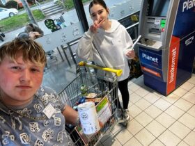 Wolontariusze biorący udział w akcji "Wielkanocna Zbiórka Żywności" zbierają żywność w sklepie Biedronka w Górze. Na zdjęciu widać koszyk z zebraną żywnością oraz wolontariuszy z ulotkami i puszką.