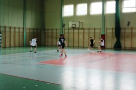 Jedną z atrakcji "Dnia sportu" był turniej piłki nożnej halowej. Zdjęcie jednego z meczów turniejowych. Zawodnicy jednej z drużyn rozgrywają akcję podaniami w środku pola, sytuacja 2 na 3.
