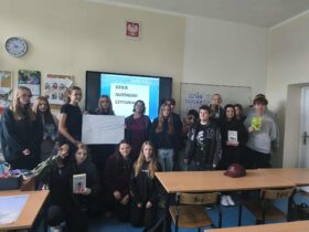 Grupowe zdjęcie uczniów z książkami w rękach, w tle widać napisy przypominające o udziale w akcji "Dzień Głośnego Czytania".